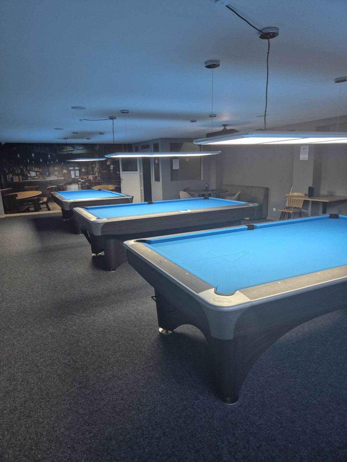Drei Billardtische mit blauen Filzdecken in einem hellen Raum.